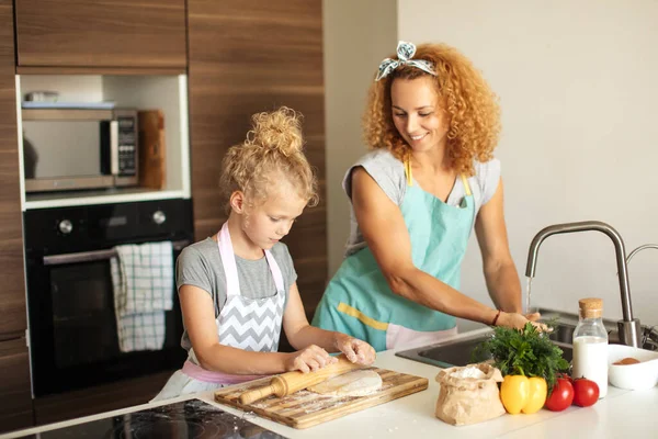 Belle jeune maman et sa mignonne petite fille déroulant la pâte à la maison. — Photo