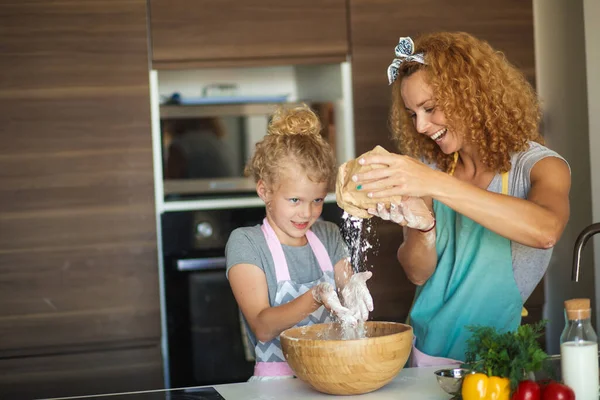 Niña y su madre rociando harina en un tazón y sonriendo mientras hornean — Foto de Stock