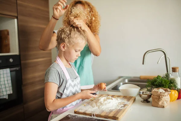 Little girl learn to make dough and her caring mother tying her hair up. — Stock Photo, Image