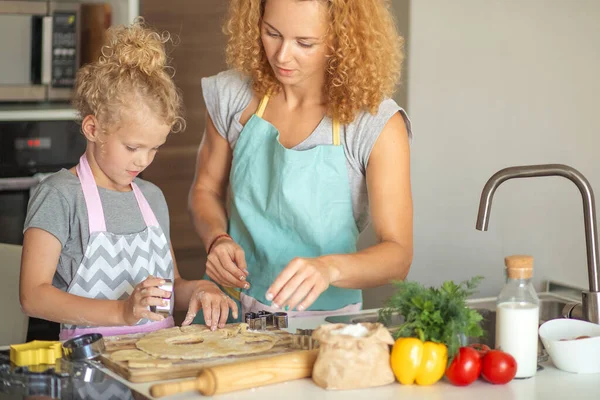 Piękna młoda mama i jej urocza córeczka zwijają ciasto w domu. — Zdjęcie stockowe