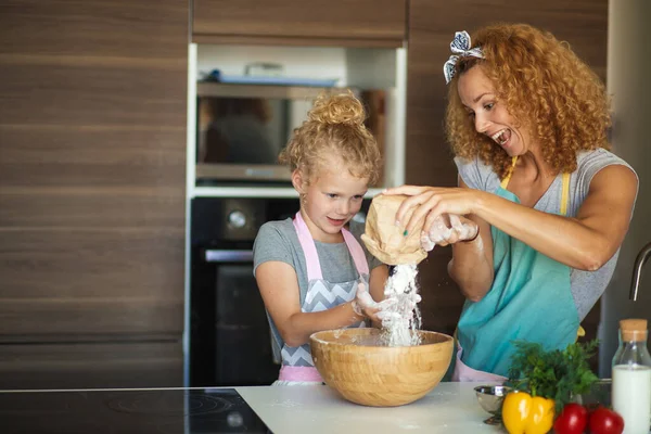 Niña y su madre rociando harina en un tazón y sonriendo mientras hornean —  Fotos de Stock