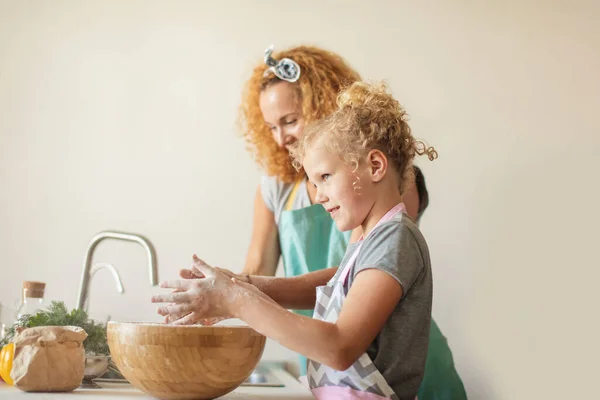 Menina e sua mãe polvilhando farinha em uma tigela e sorrindo ao assar — Fotografia de Stock