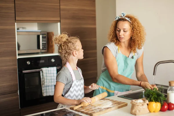 Belle jeune maman et sa mignonne petite fille déroulant la pâte à la maison. — Photo