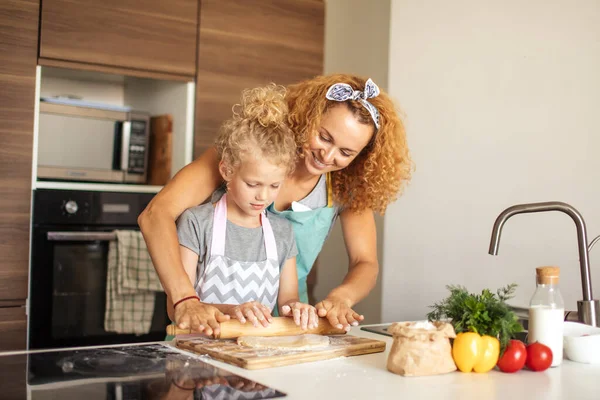 Hübsch jung mutter und sie süß klein tochter rolling out teig at home. — Stockfoto