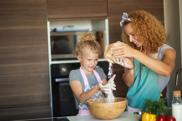 Niña y su madre rociando harina en un tazón y sonriendo mientras hornean —  Fotos de Stock