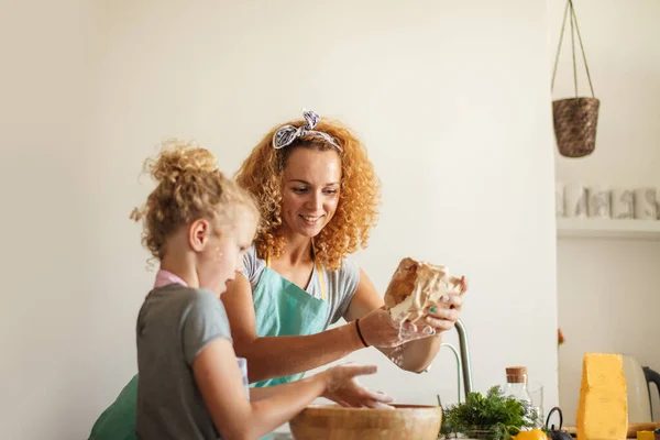 Маленькая девочка и ее мать поливают муку в миску и улыбаются во время выпечки — стоковое фото
