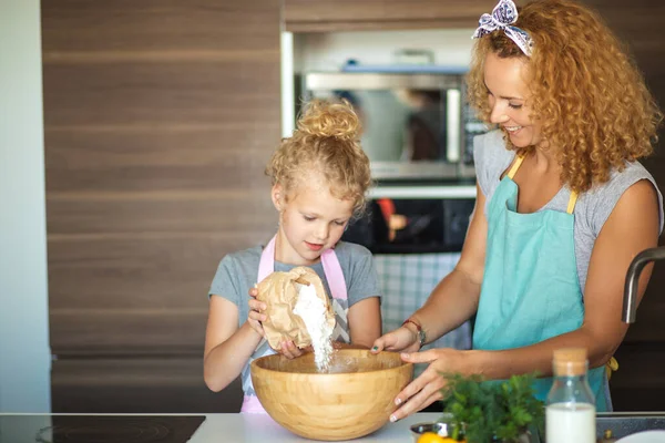 Kleines Mädchen und ihre Mutter streuen Mehl in eine Schüssel und lächeln beim Backen — Stockfoto