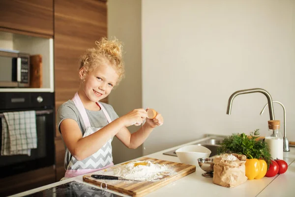 女の子立っていますで作物の母親とクラッキング卵へ小麦粉オンキッチン. — ストック写真