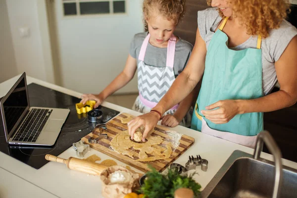 Child and women cutting form for cookie in dough. Happy family and childhood.