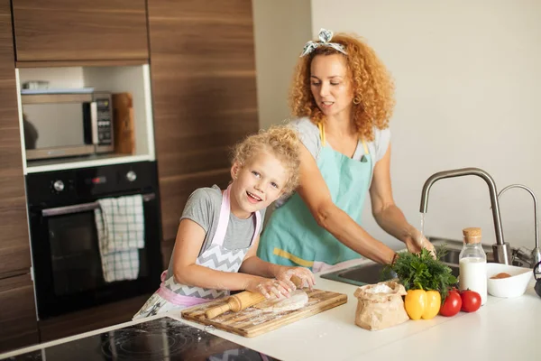 Hübsch jung mutter und sie süß klein tochter rolling out teig at home. — Stockfoto