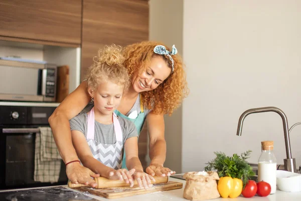 Hermosa mamá joven y su linda hijita rodando la masa en casa. — Foto de Stock