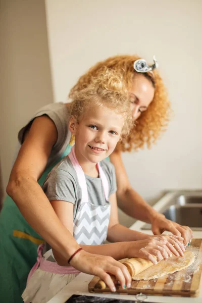 Piękna młoda mama i jej urocza córeczka zwijają ciasto w domu. — Zdjęcie stockowe