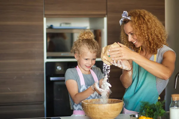Niña y su madre rociando harina en un tazón y sonriendo mientras hornean —  Fotos de Stock