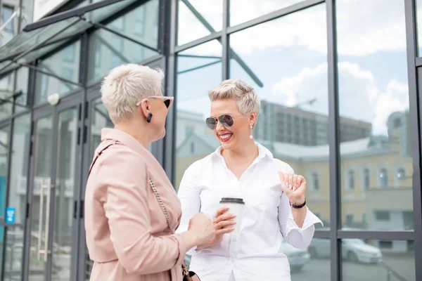 Two businesswomen standing outside with coffee with buildings on background — Stock Photo, Image