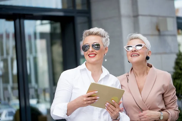 Two businesswoman walking on street near building. business woman going together with tablet computer — Stock Photo, Image