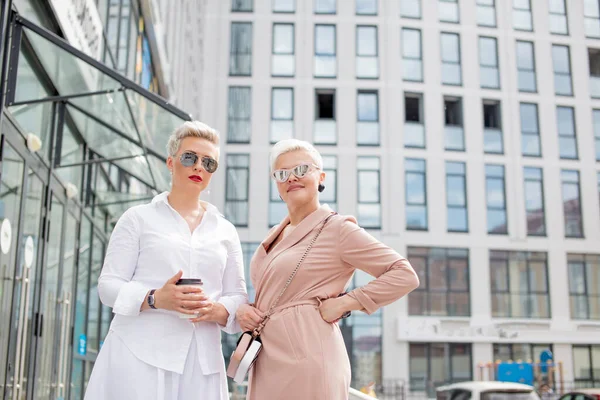 Två affärskvinnor står utanför med kaffe med byggnader på bakgrunden — Stockfoto