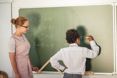 Çocuk toplama ve çıkarma işlemlerini çözüyor. okul çocuğu matematiksel işlemin yazım çözümü