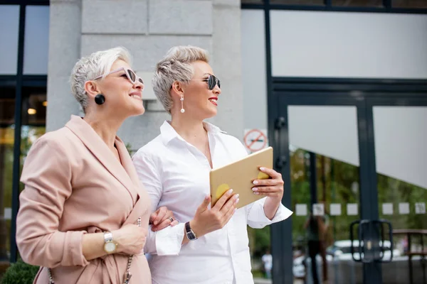 Two businesswoman walking on street near building. business woman going together with tablet computer — Stock Photo, Image