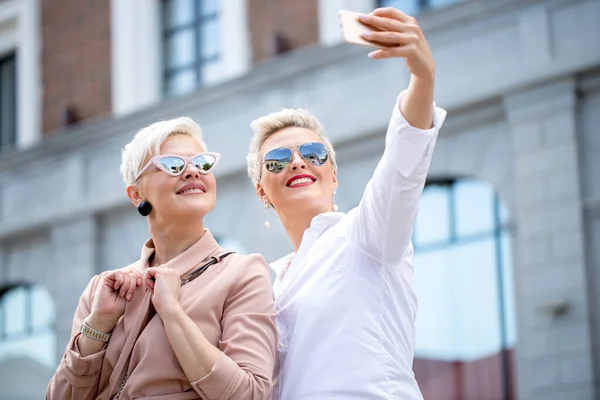 Stijlvolle volwassen zakenvrouwen poseren voor selfie buiten in de buurt van kantoorgebouw — Stockfoto
