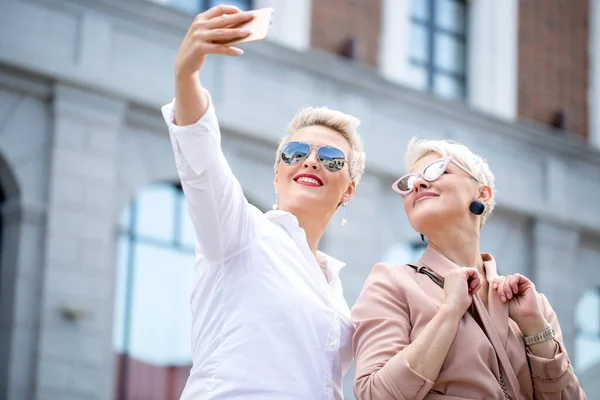 Stijlvolle volwassen zakenvrouwen poseren voor selfie buiten in de buurt van kantoorgebouw — Stockfoto