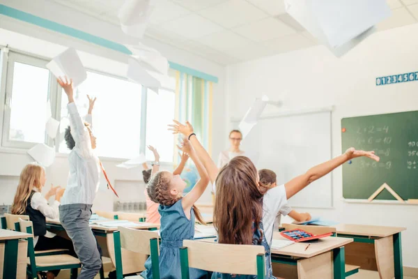 Los niños de la escuela se divierten en clase y tiran papel al aire —  Fotos de Stock