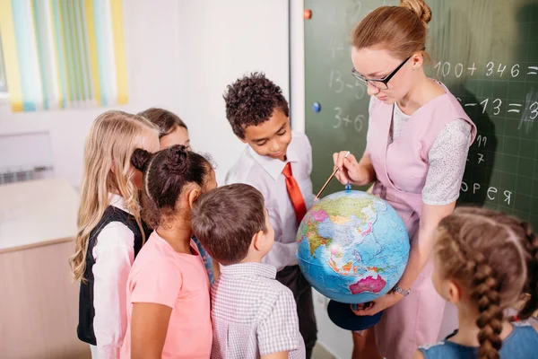 Школьники смотрят на земной шар с учителем на уроке географии — стоковое фото