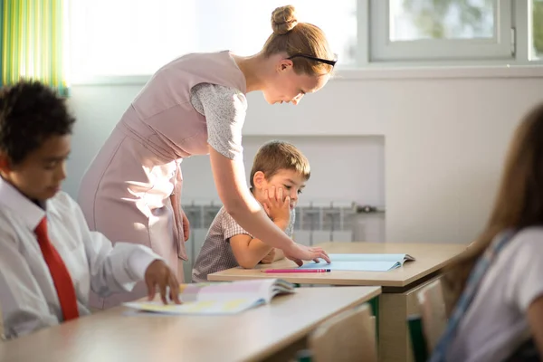 Professor ajudando crianças com seus trabalhos de casa em sala de aula na escola — Fotografia de Stock