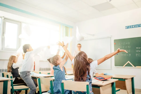 Los niños de la escuela se divierten en clase y tiran papel al aire —  Fotos de Stock