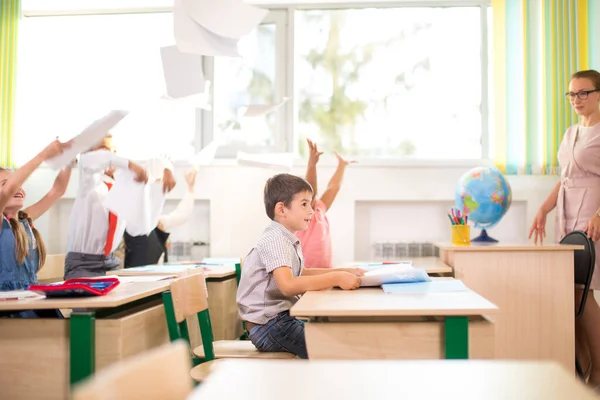 Los niños de la escuela se divierten en clase y tiran papel al aire — Foto de Stock
