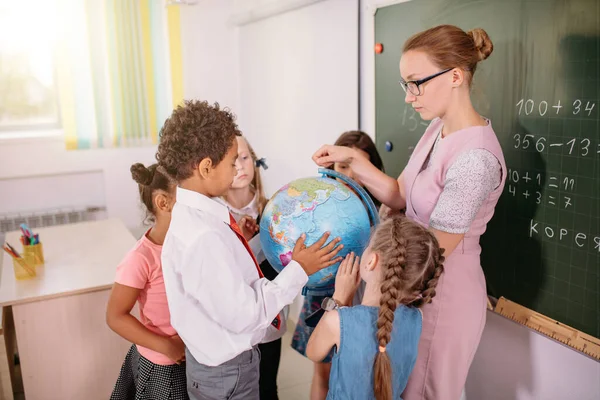 Escolares mirando el globo con el profesor en la lección de geografía —  Fotos de Stock
