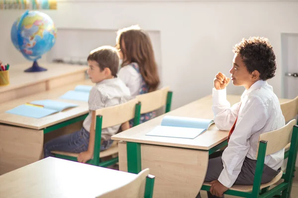 Niño de la escuela sentado en el escritorio y pensando mientras escribe examen —  Fotos de Stock