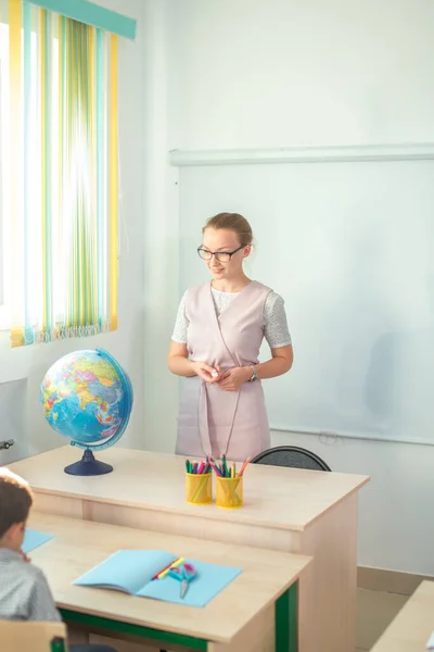 Молодая учительница смотрит в сторону стола с глобусом — стоковое фото