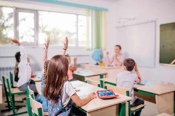 Groep schoolkinderen die allemaal hun handen in de lucht steken om te antwoorden — Stockfoto