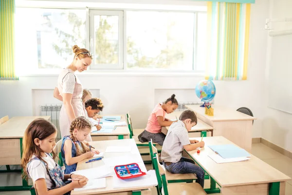 Учитель помогает детям с домашним заданием в классе в школе — стоковое фото