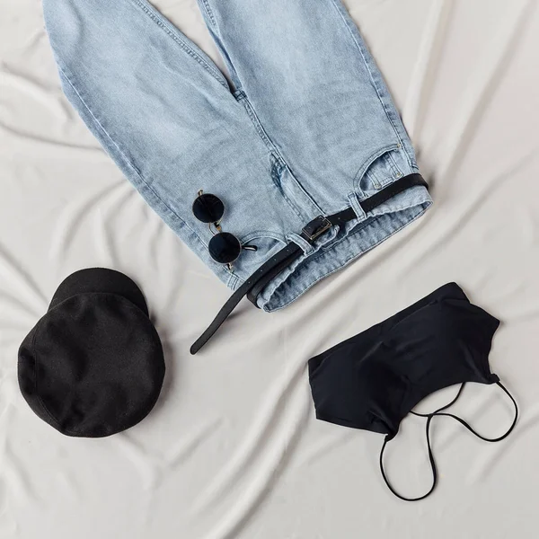 Блузка, кепка, джинсы с ремнем, лежащие на белом листе — стоковое фото