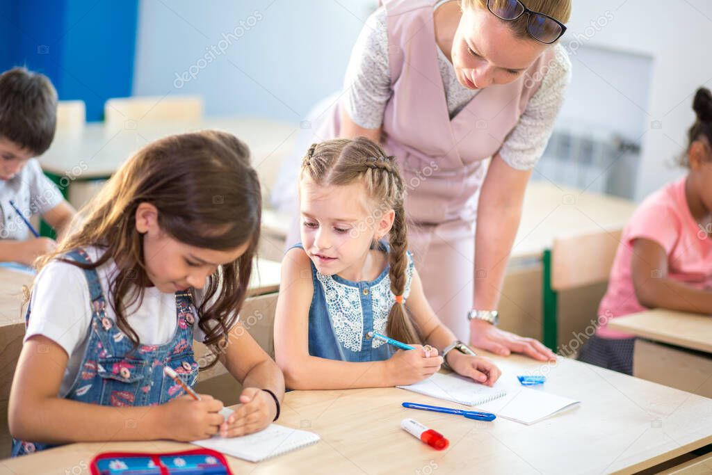 Teacher helping kids with their homework in classroom at school