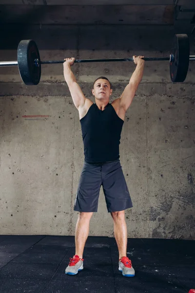 Atleta impresionante levanta la barra sobre su cabeza. — Foto de Stock