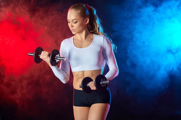 Serious woman in stylish sportswear working out with dumbbells — Stock Photo, Image