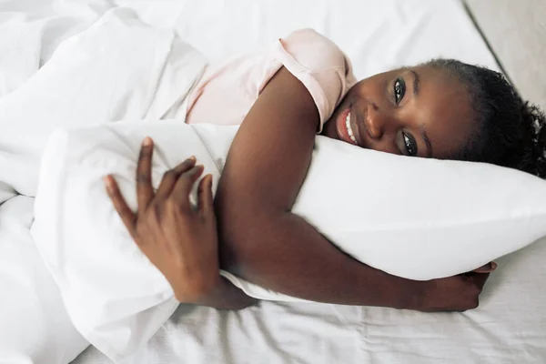 Positive charmante Mädchen umarmt ein Kissen und schaut in die Kamera — Stockfoto