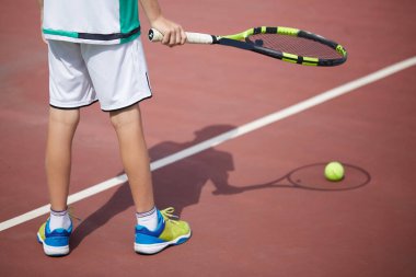 Erkek eli kırmızı kil kortta tenis topu ve raket tutuyor..