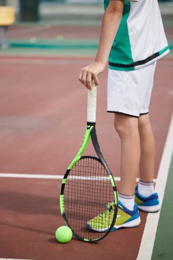 Erkek eli kırmızı kil kortta tenis topu ve raket tutuyor..