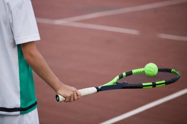 Erkek eli kırmızı kil kortta tenis topu ve raket tutuyor..