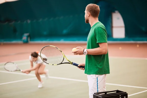 Hombre barbudo joven en ropa deportiva verde está jugando al tenis en la cancha cubierta. — Foto de Stock