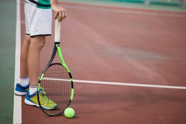 Erkek eli kırmızı kil kortta tenis topu ve raket tutuyor..