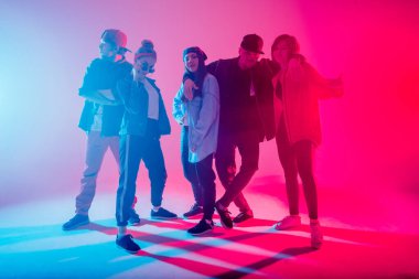 Stüdyoda kırmızı ve mavi çift renkli ışıkla dans eden bir grup insan.