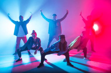 Stüdyoda kırmızı ve mavi çift renkli ışıkla dans eden bir grup insan.