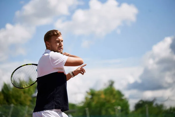 Junger Mann in Sportbekleidung spielt Tennis auf Außenplatz. — Stockfoto