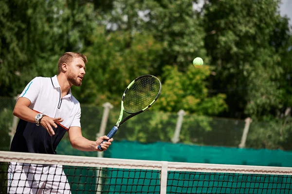 Joven en ropa deportiva está jugando al tenis en la pista de al aire libre. — Foto de Stock