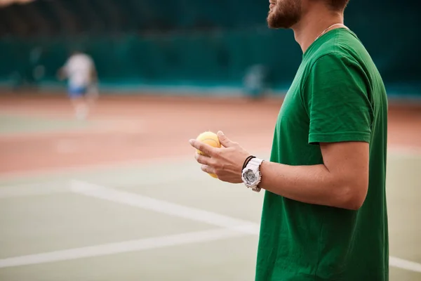 Jovem barbudo em sportwear verde está jogando tênis na quadra interna . — Fotografia de Stock
