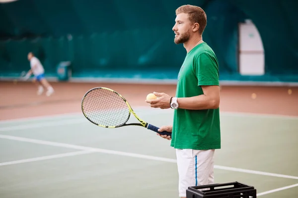 Młody brodaty mężczyzna w zielonym stroju sportowym gra w tenisa na korcie. — Zdjęcie stockowe